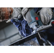 Mann schneidet Metall mit einer Stichsäge. Er trägt Schutzbrille, Atemschutzmaske und Handschuhe.