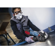 Mann arbeitet mit einem Winkelschleifer auf einem Bodenbelag, persönliche Schutzausrüstung ist vorhanden