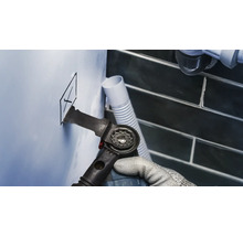 Handwerker schneidet mit einem Multifunktionswerkzeug ein Loch in eine Wand