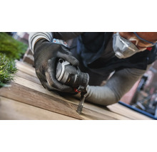 Ein Mann verwendet ein Multifunktionswerkzeug mit Sägeblatt auf einem Holzbrett.