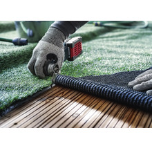 Verlegen von Kunstrasen mit Werkzeug auf einer Holzterrasse.