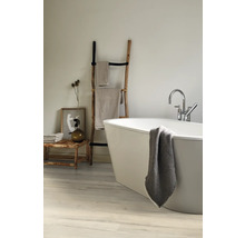 Helles Badezimmer mit freistehender Badewanne, Handtüchern auf einer Holzleiter und einer Holzbank mit Dekorationen