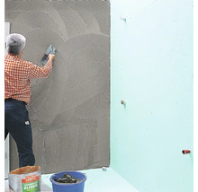 Ein Handwerker trägt Fliesenkleber auf eine Wand im Badezimmer auf.