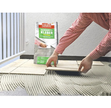 Eine Person verlegt Fliesen mit Fliesenkleber der Marke Lugato.