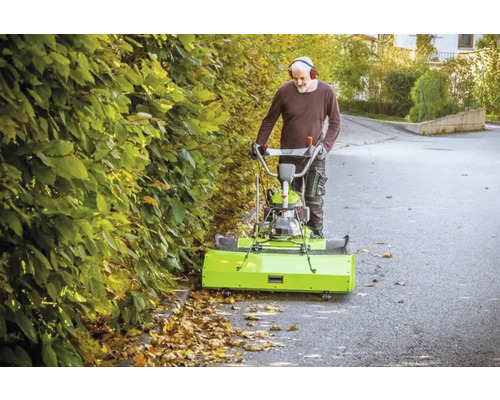 Mann benutzt eine Kehrmaschine zur Laubentfernung auf einer Straße.