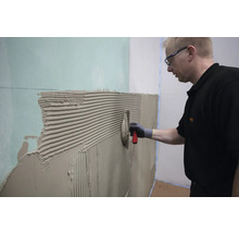 Ein Mann trägt Klebstoff mit einer Kelle auf eine Wand auf.