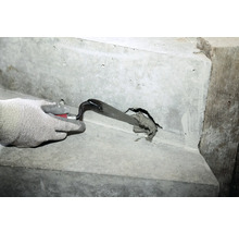 Eine Hand mit Schutzhandschuh verschließt ein Loch in einer Betontreppe mit einer Maurerkelle und Fugenmasse.