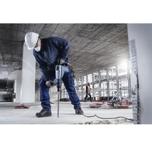 Ein Bauarbeiter bohrt mit einem Bohrhammer in einen Betonboden.