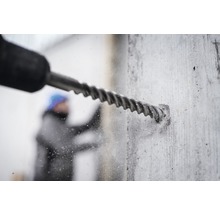 Nahaufnahme einer Bohrmaschine beim Bohren eines Lochs in eine Betonwand.