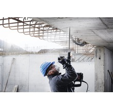 Ein Bauarbeiter bohrt mit einem Bohrhammer in eine Betondecke.