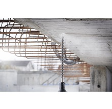 Ein Bohrer bohrt in eine Betonwand, umgeben von Bewehrungsstahl.