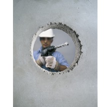 Ein Arbeiter bohrt mit einem Bohrhammer ein Loch in eine Betonwand.