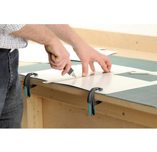 Zuschneiden einer Kunststoffplatte mit einem Cuttermesser und einem Lineal, fixiert mit einer Zwinge.