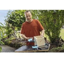 Mann baut ein Vogelhaus mit Schraubzwingen auf einer Werkbank im Garten.