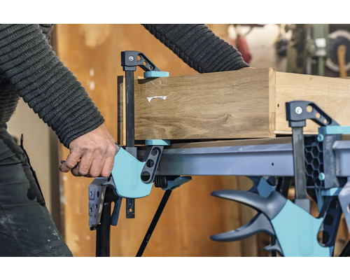 Handwerker fixiert Holz mit einer Einhandzwinge auf einem Werktisch