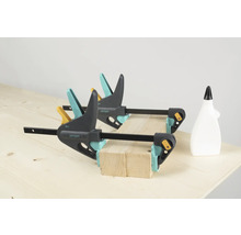 Zwei Wolfcraft Einhandzwingen fixieren Holzstücke auf einer Werkbank, eine Flasche Leim steht daneben.