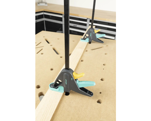 Zwei Wolfcraft Einhandzwingen fixieren ein Werkstück auf einer Werkbank.