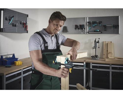 Mann fixiert Holzstücke mit einer Einhandzwinge in einer Werkstatt.