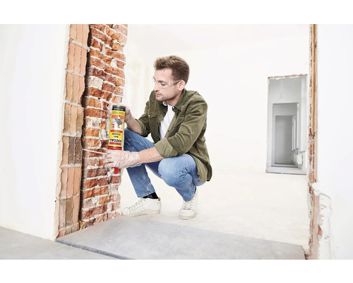 Mann trägt Bauschaum von Soudal auf eine Backsteinmauer auf.