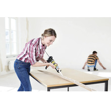 Frau trägt Klebstoff mit einer Pistole auf Holzleiste auf einem Tisch auf