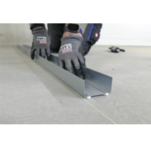 Eine Person befestigt ein Metallprofil mit Klebstoff auf einem Boden.