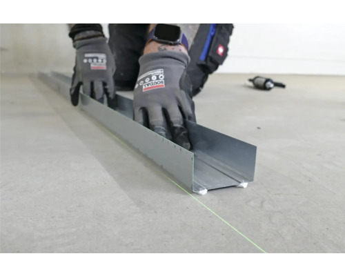 Eine Person befestigt ein Metallprofil mit Klebstoff auf einem Boden.