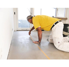 Mann klebt Abdeckband auf einem Boden für Renovierungsarbeiten.