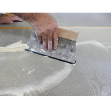 Ein Handwerker verteilt Klebstoff mit einem Spachtel.