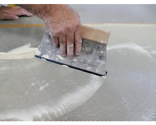 Ein Handwerker verteilt Klebstoff mit einem Spachtel.