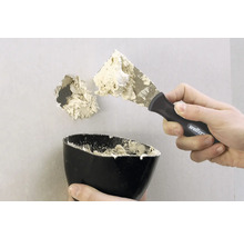 Ein Loch in einer Wand wird mit einem Spachtel und Spachtelmasse repariert.