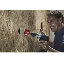 Ein Mann bohrt mit einer Lochsäge ein Loch in eine Holzplatte.