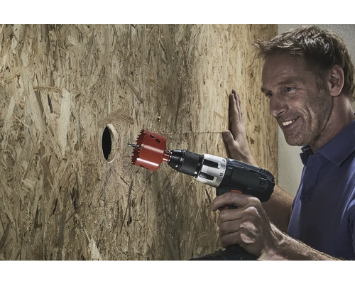 Ein Mann bohrt mit einer Lochsäge ein Loch in eine Holzplatte.