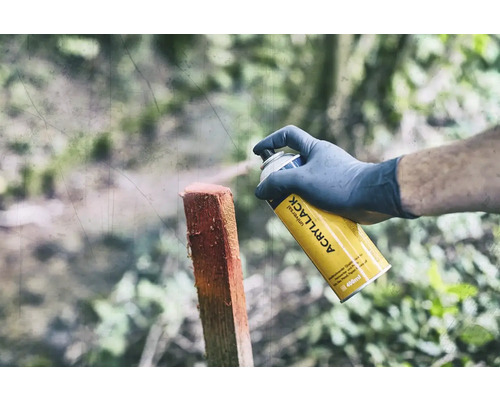 Eine Person sprüht mit einer gelben Universalspraydose einen Holzpfosten an