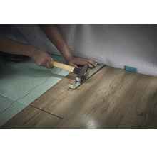 Person verlegt Laminat mit Zugeisen und Hammer
