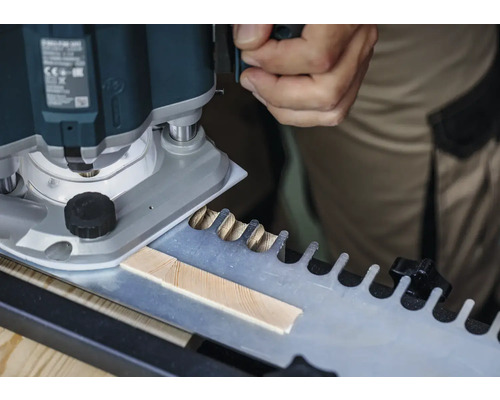 Eine Oberfräse beim Bearbeiten eines Werkstücks mit einer Schablone für Zinkenverbindungen.