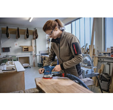 Frau schleift Holzbrett mit Exzenterschleifer in Werkstatt