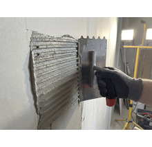 Fliesenkleber wird mit einer rostfreien Stahltraufel an einer Wand aufgetragen