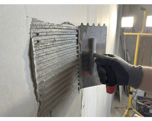 Fliesenkleber wird mit einer rostfreien Stahltraufel an einer Wand aufgetragen