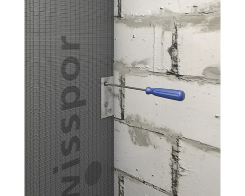 Ein Schraubendreher fixiert eine Metallplatte an einer grauen Bauplatte an einer weißen Mauer.