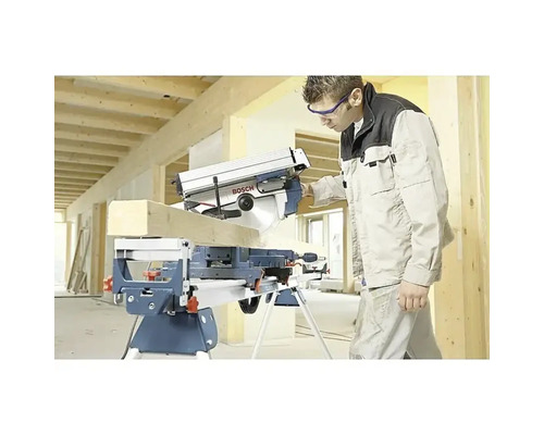 Handwerker schneidet Holzbalken mit einer Bosch Kapp- und Gehrungssäge auf einem Arbeitstisch in einem hellen Rohbau.