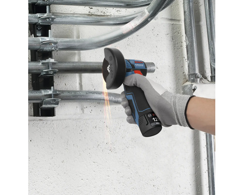 Bosch Professional 12 Volt Akku-Winkelschleifer trennt ein Metallrohr an einer Wand mit sichtbarem Funkenflug.