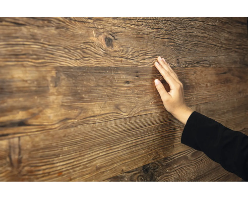 Hand berührt eine rustikale Holzoberfläche mit ausgeprägter Maserung und Struktur.