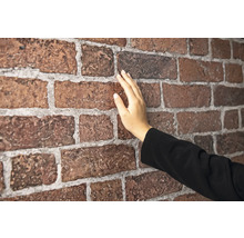 Eine Hand berührt eine Wand aus Verblendern in Backsteinoptik mit fühlbarer Oberflächenstruktur und Fugen.