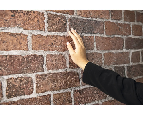Eine Hand berührt eine Wand aus Verblendern in Backsteinoptik mit fühlbarer Oberflächenstruktur und Fugen.