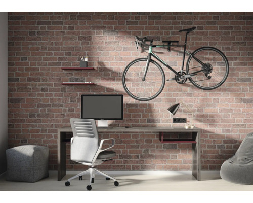 Industrieller Raum mit Wand in Backsteinoptik, Schreibtisch mit Computer, Bürostuhl und an der Wand montiertem Fahrrad.
