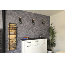 Wohnraum mit einer Wand in Steinoptik, einem weißen Sideboard, drei Wandleuchten im Industriedesign und einem Kaminholzregal.