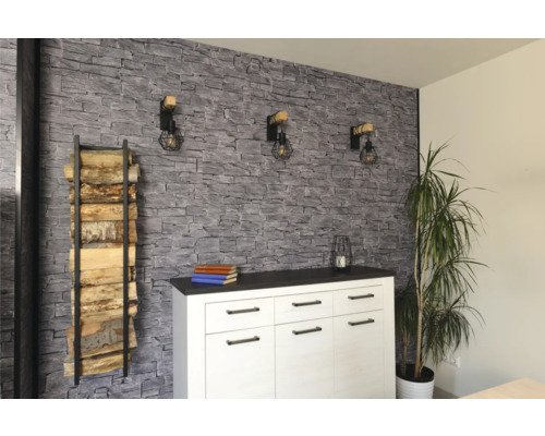 Wohnraum mit einer Wand in Steinoptik, einem weißen Sideboard, drei Wandleuchten im Industriedesign und einem Kaminholzregal.