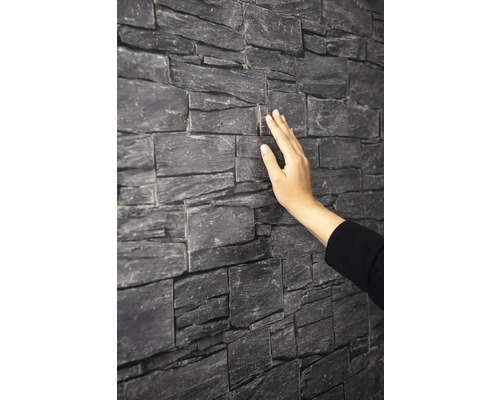 Wandverkleidung in Natursteinoptik mit strukturierter Oberfläche, die von einer Hand berührt wird.