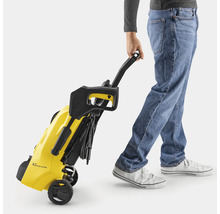 Eine Person zieht einen gelben Kärcher Hochdruckreiniger K3 Power Control am schwarzen Griff. Das Gerät wird auf Rollen transportiert.