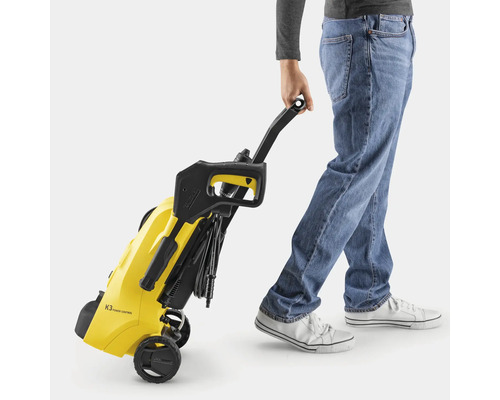 Eine Person zieht einen gelben Kärcher Hochdruckreiniger K3 Power Control am schwarzen Griff. Das Gerät wird auf Rollen transportiert.